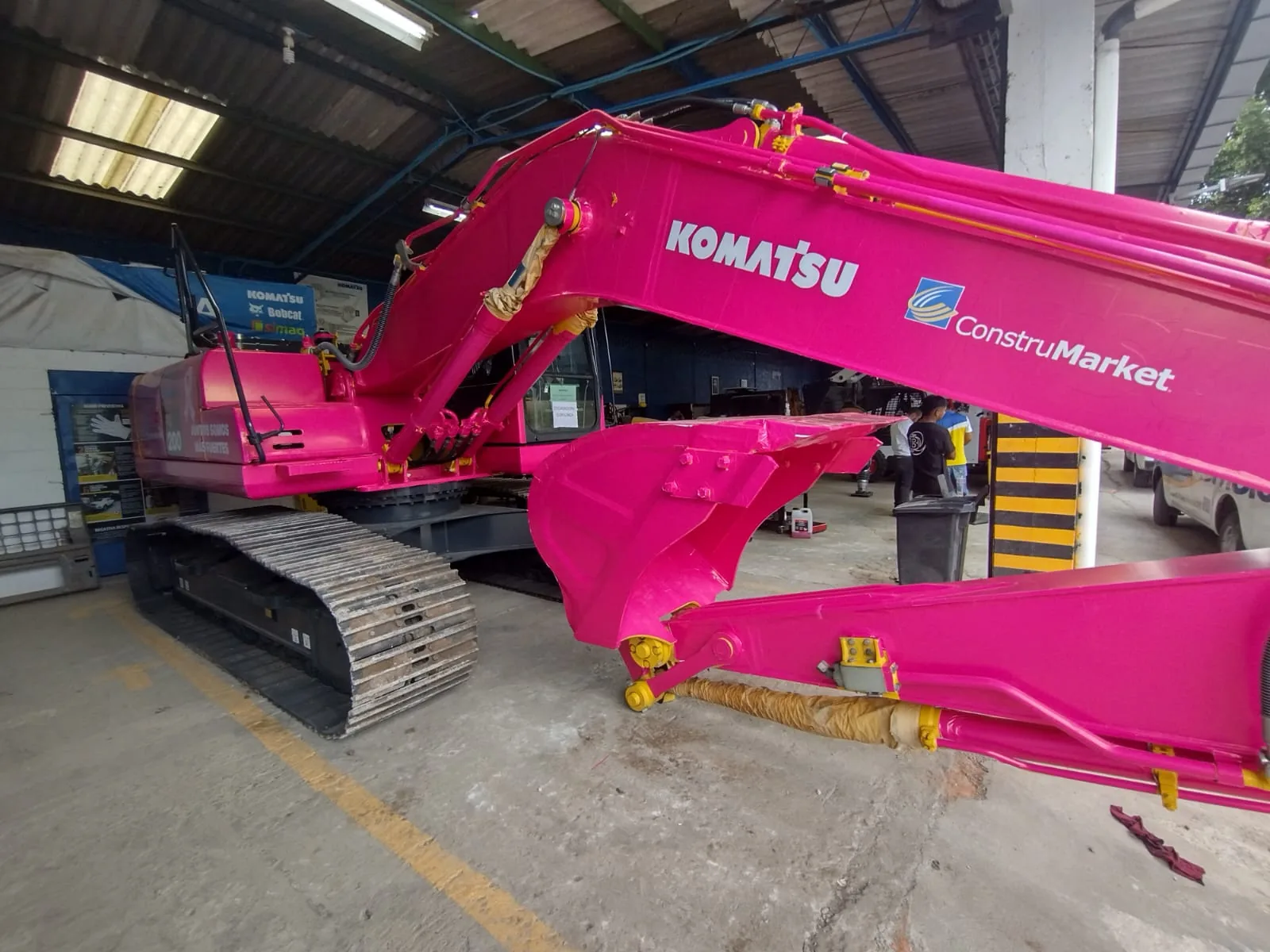 Bright pink Komatsu excavator inside the workshop, with the Komatsu and ConstruMarket logos on the boom