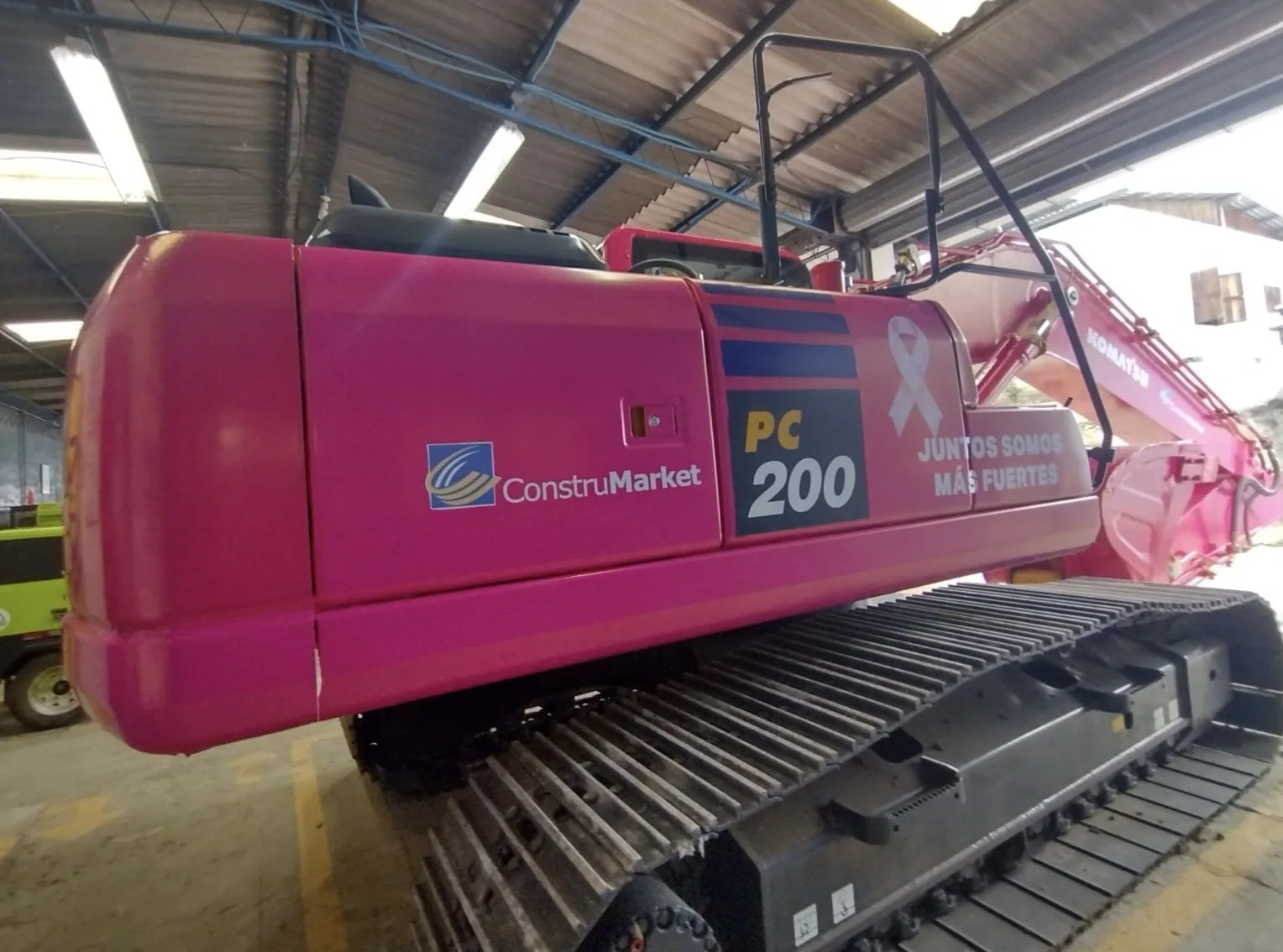 Pink Komatsu PC200 excavator with the campaign ribbon and the message “Together we are stronger”