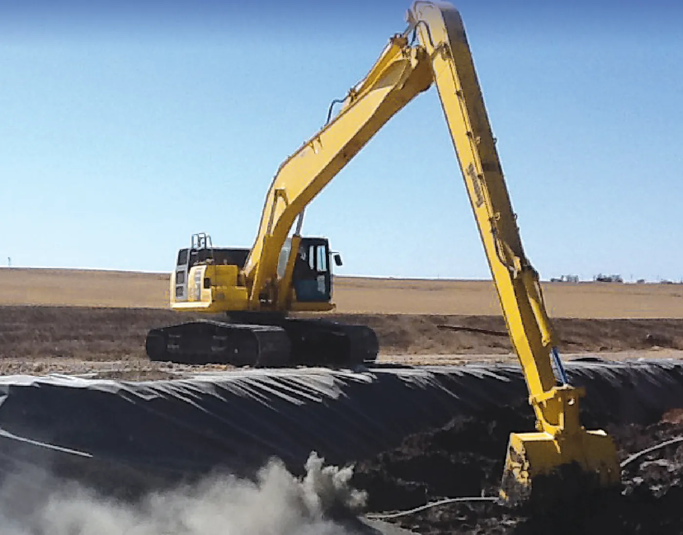 Excavadora Komatsu con Super Long Front trabajando desde la orilla firme sobre una laguna revestida, sin meter la máquina al agua